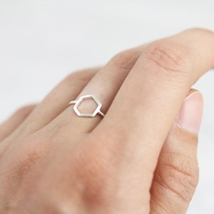 May include: A silver ring featuring a hexagonal design. The ring is worn on a finger.