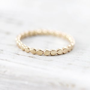May include: A delicate gold ring with a beaded design. The ring is made of small, round beads that are evenly spaced along the band.