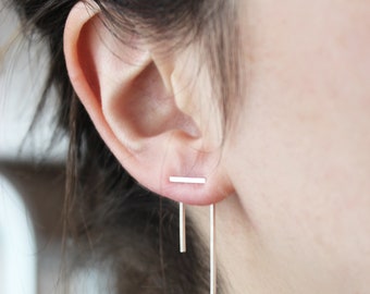 Puede incluir: Pendientes de barra de plata con una barra larga y fina que cuelga de la barra superior. Los pendientes se llevan en el lóbulo de la oreja.
