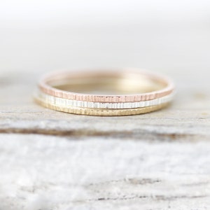 May include: Three thin gold rings stacked on top of each other. The top ring is rose gold, the middle ring is yellow gold, and the bottom ring is silver.