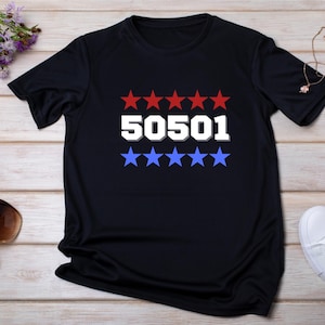 Peut inclure: T-shirt noir avec le numéro "50501" en blanc, encadré d'étoiles rouges au-dessus et d'étoiles bleues en dessous. Le t-shirt est présenté sur une surface en bois clair, avec des accessoires comme des lunettes de soleil et des chaussures.