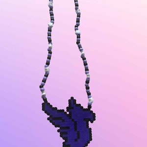 Puede incluir: Un collar de cuentas con un colgante de rayo morado oscuro. El collar tiene una hebra de pequeñas cuentas redondas en negro, morado y estrellas blancas. El colgante es un diseño pixelado.