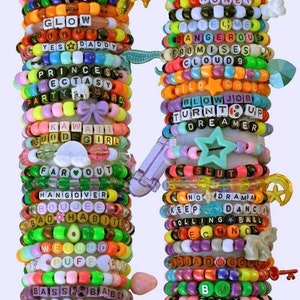 May include: A stack of colorful beaded bracelets with various words and phrases, including "I Bite", "Glow", "Yes Daddy", "Princess", "Kawaii", "Far Out", "Hangover", "Boujee", "Bad Habits", "Weird", "Puff", "Bass", "Nice Ass", "Boobs", "Honey", "Hate Me", "Dangerous", "Promises", "Cloud 9", "Wild Child", "Blow Job", "Turn It Up", "Dreamer", "Slut", "No Drama", "Keep Dancing", "Rolling Ball", "Techno", "Squad Goals", "BJ", "Sassy", and "Juicy".