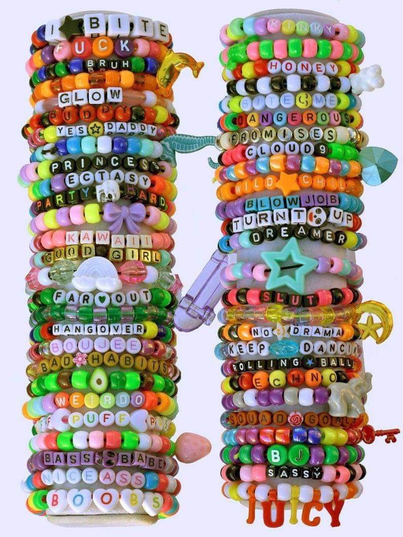 May include: A stack of colorful beaded bracelets with various words and phrases, including "I Bite", "Glow", "Yes Daddy", "Princess", "Kawaii", "Far Out", "Hangover", "Boujee", "Bad Habits", "Weird", "Puff", "Bass", "Nice Ass", "Boobs", "Honey", "Hate Me", "Dangerous", "Promises", "Cloud 9", "Wild Child", "Blow Job", "Turn It Up", "Dreamer", "Slut", "No Drama", "Keep Dancing", "Rolling Ball", "Techno", "Squad Goals", "BJ", "Sassy", and "Juicy".