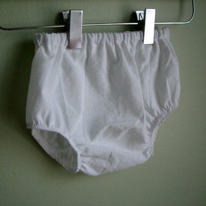May include: White cotton baby bloomers hanging on a clothes hanger.