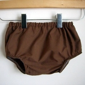 May include: Brown cotton baby bloomers hanging on a wooden hanger with metal clips.