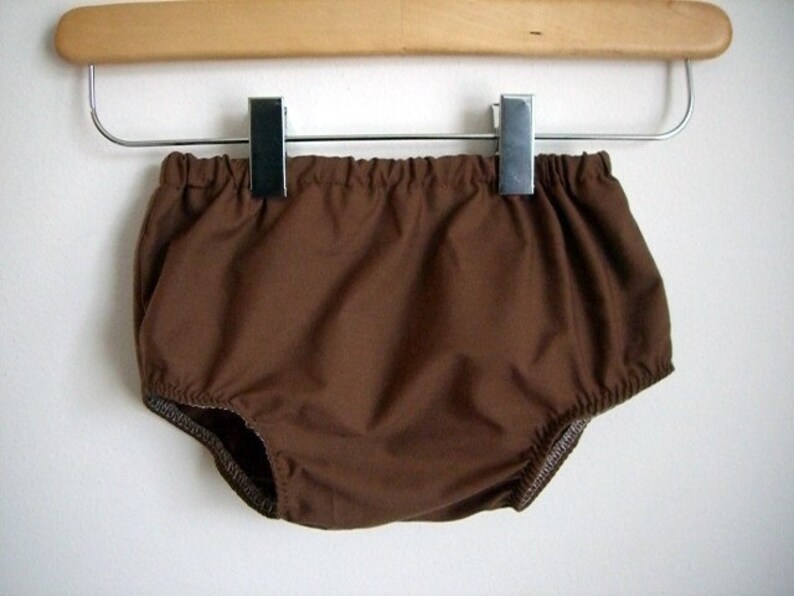 May include: Brown cotton baby bloomers hanging on a wooden hanger with metal clips.