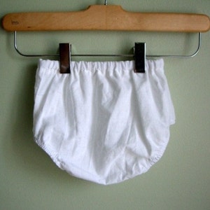 May include: White cotton baby bloomers hanging on a wooden hanger with silver clips.