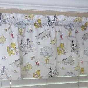 May include: A white valance featuring a repeating pattern of Winnie the Pooh characters, including Pooh Bear, Eeyore, and Tigger, with trees and butterflies. The valance is mounted on a dark brown curtain rod.