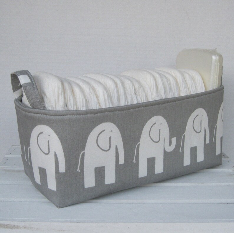 May include: A gray fabric storage bin with a white elephant pattern. The bin is filled with diapers and has a white plastic lid.