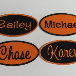 Puede incluir: Cuatro parches ovalados con nombres. Dos parches tienen fondos negros con letras naranjas, y dos tienen fondos naranjas con letras negras. Los nombres "Bailey" y "Karen" est&aacute;n en los fondos negros, y "Michael" y "Chase" en los fondos naranjas.