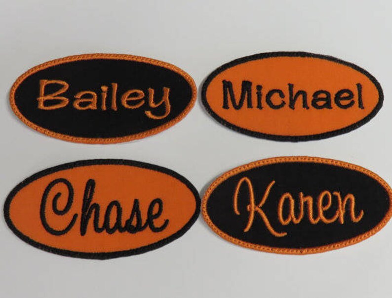 Puede incluir: Cuatro parches ovalados con nombres. Dos parches tienen fondos negros con letras naranjas, y dos tienen fondos naranjas con letras negras. Los nombres "Bailey" y "Karen" est&aacute;n en los fondos negros, y "Michael" y "Chase" en los fondos naranjas.