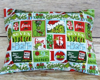 May include: A green and red fabric pillow with a repeating pattern of the Grinch and the words "12 Days of Grinchmas".