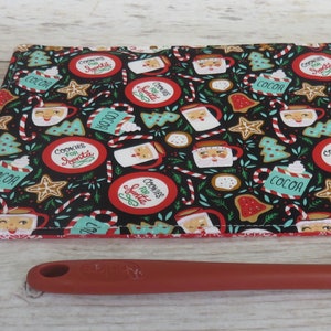 May include: A black and red Christmas-themed hot pad with a pattern of Santa Claus, candy canes, and mugs of hot cocoa. The hot pad is on a wooden surface with a sign that says "happy home".