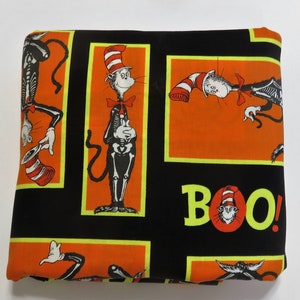 May include: Black fabric with a repeating pattern of a skeleton cat wearing a red and white hat. The cat is holding a red bow tie. The fabric also has a repeating pattern of an orange rectangle with the word "BOO!" in yellow letters.