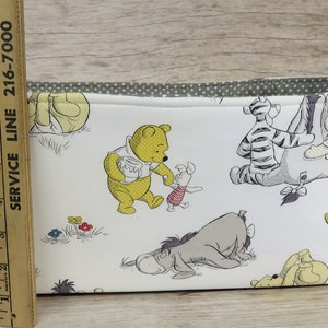 May include: White fabric storage bin with a yellow ribbon handle. The bin features a Winnie the Pooh theme with illustrations of Winnie the Pooh, Piglet, Eeyore, Tigger, and other characters from the Disney cartoon.