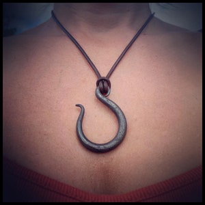 May include: A brown leather necklace with a large, silver, hook-shaped pendant.