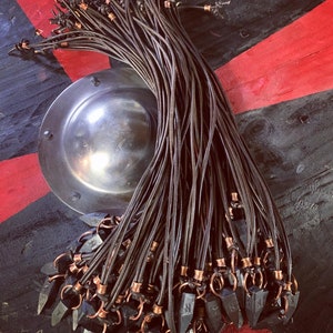 Op de afbeelding: Een bundel zwarte leren koorden met koperen accenten en zwarte metalen pijlpunt hangers. De koorden zijn aan de bovenkant aan elkaar gebonden en de pijlpunten hangen naar beneden.