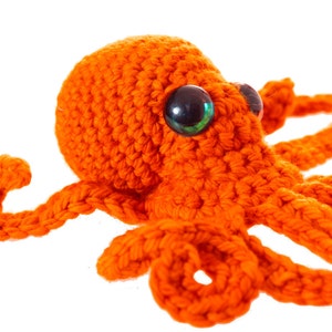 May include: A crocheted orange octopus with green eyes. The octopus has eight tentacles and is made of yarn.