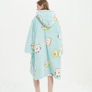 May include: A light blue hooded blanket with a pattern of cartoon avocados and toast. The blanket is worn by a person standing on a white background.