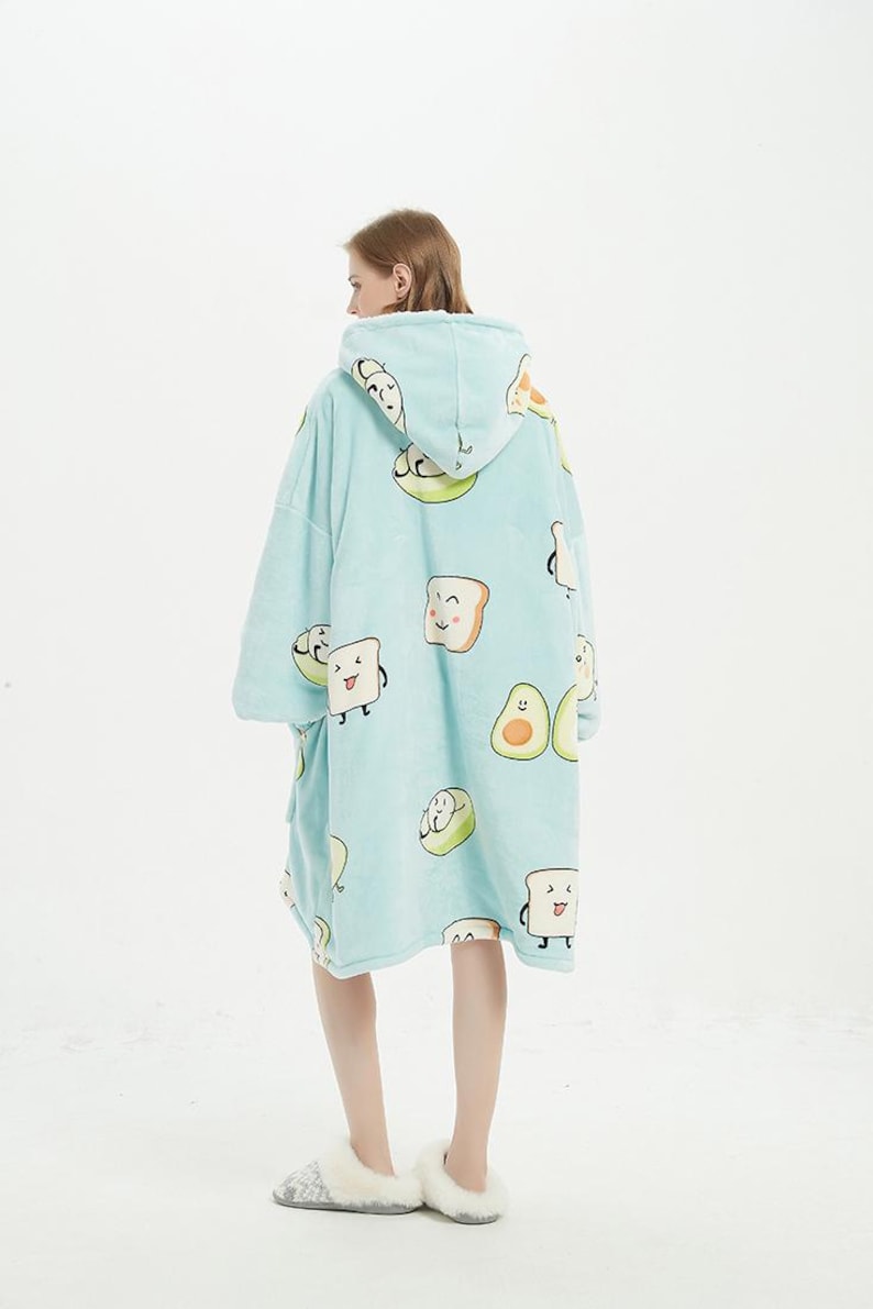 May include: A light blue hooded blanket with a pattern of cartoon avocados and toast. The blanket is worn by a person standing on a white background.