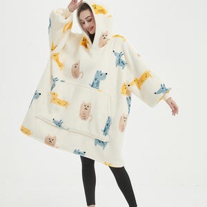May include: A white hooded blanket with a print of cartoon cats and dogs. The blanket has a large pocket on the front.