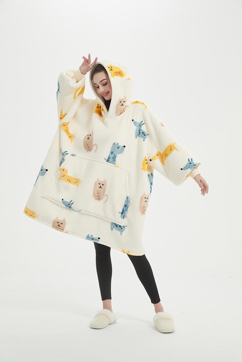 May include: A white hooded blanket with a print of cartoon cats and dogs. The blanket has a large pocket on the front.