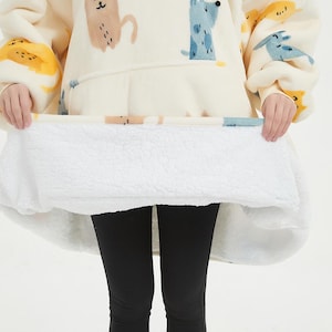 May include: A white hooded blanket with a plush white lining. The blanket features a cartoon animal print with yellow, blue, and brown colors.