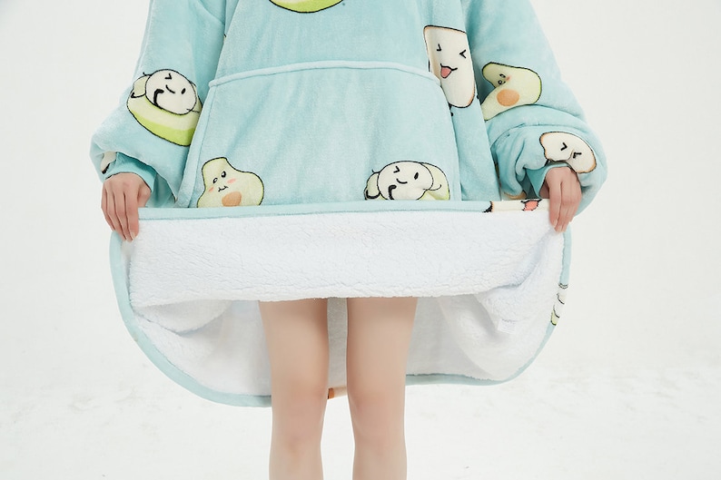 May include: A light blue hooded blanket with a white sherpa lining. The blanket features a cartoon avocado print with smiling faces.