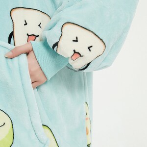 May include: A light blue fleece robe with a white and black cartoon design of bread and avocado. The robe has a hood and a front pocket.