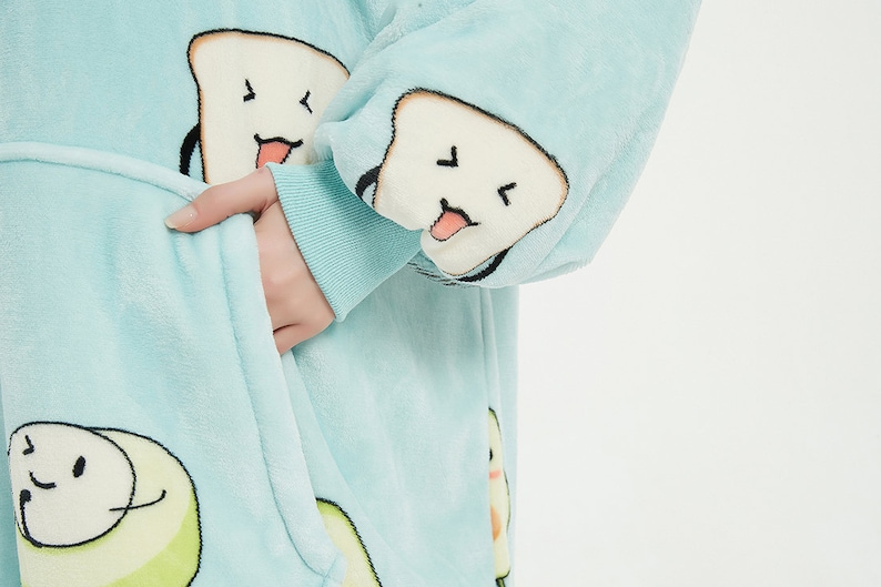 May include: A light blue fleece robe with a white and black cartoon design of bread and avocado. The robe has a hood and a front pocket.
