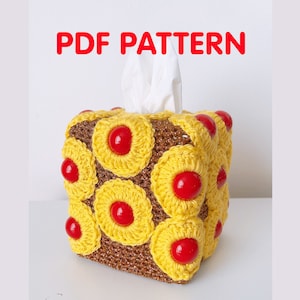 Può includere: Copertura per scatola di fazzoletti all'uncinetto con un design a ananas giallo e rosso. La copertura è realizzata con un filo marrone e ha una superficie testurizzata. La copertura è etichettata "PDF PATTERN".