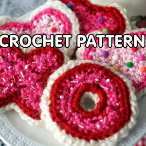 May include: Crochet pattern for a set of three Valentine's Day themed cookies. The cookies are shaped like hearts and a donut, and are decorated with pink, red and white yarn. The text "CROCHET PATTERN" is visible in the image.