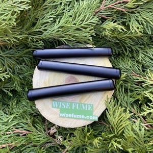 Puede incluir: Tres tubos cilíndricos negros con extremos redondeados, dispuestos sobre una superficie de madera. Los tubos están etiquetados con "WISE FUME" y "wisefume.com".