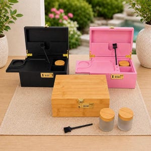May include: Three wooden boxes, one bamboo and two painted black and pink, with combination locks. The boxes are open, revealing compartments and tools. Two glass jars with wooden lids and a small brush are also present.