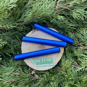 May include: Three blue metal tubes with rounded ends, arranged on a wooden surface. The tubes are labeled "WISE FUME" with the website "wisefume.com" printed below.