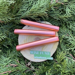 May include: Three rose gold metal tubes with a logo sticker that reads "WISE FUME" and "wisefume.com" on a wooden surface.