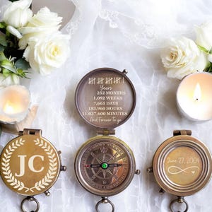 May include: Three brass compasses with custom engravings. One shows tally marks and time units including 252 months and 11,037,600 minutes. Another features the initials JC inside a laurel wreath. The third displays June 27, 2004 and an infinity symbol.