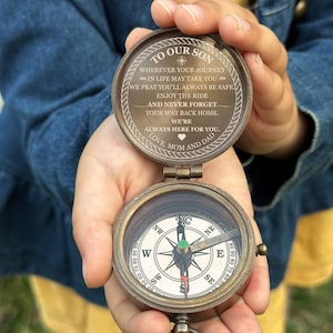 May include: A vintage-style brass compass, open to reveal the compass face and an engraved message. The text reads "To Our Son" followed by an inspirational message from "Love, Mom and Dad". The compass features a directional dial with cardinal directions.