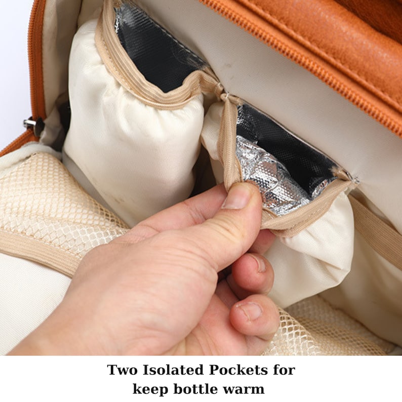 K&ouml;nnte beinhalten: Nahaufnahme des Innenraums einer braunen Wickeltasche mit zwei isolierten Taschen zum Warmhalten von Flaschen. Die Taschen sind mit silberner Folie ausgekleidet und haben Rei&szlig;verschl&uuml;sse.