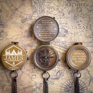 May include: Three antique compasses with intricate designs and text. One features a tent graphic and the name "JAMES", another displays the Scout Oath, and the third has a message for a leader. They are set against a vintage map background.