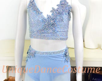 May include: A light blue dance costume displayed on a mannequin. The top is embellished with sparkling rhinestones and floral designs. The matching skirt is a sheer, flowing fabric. The text "Unique Dance Costume" is visible.