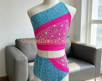 May include: A two-piece dance costume featuring a one-shoulder crop top and high-waisted briefs. The set is decorated with a diagonal color-blocked pattern of bright blue and hot pink, fully embellished with clear crystals and silver studs.