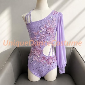 May include: A lavender dance leotard featuring an asymmetrical neckline, one long sheer sleeve, and a cutout at the waist. The garment is embellished with scattered crystals and floral lace appliqués. The text UniqueDanceCostume is visible.