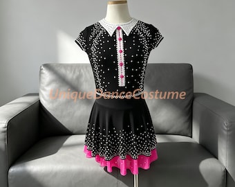 May include: A black dance costume featuring a white collar, short sleeves, and a flared skirt. The bodice and skirt are adorned with scattered clear crystals. A vertical white placket with four bright pink buttons runs down the center front.