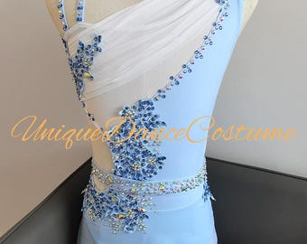 May include: A light blue dance costume with white mesh and intricate blue and silver embellishments. The costume features a one-shoulder design and is adorned with sparkling details. The text "Unique Dance Costume" is visible on the front.