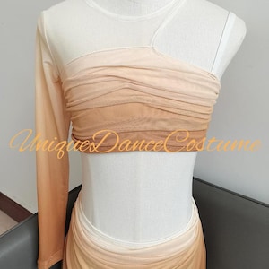 May include: A two-piece dance costume featuring a long-sleeve asymmetrical crop top and a matching skirt, both crafted from ruched mesh fabric in an ombre gradient of beige, tan, and brown tones. The text UniqueDanceCostume is visible.