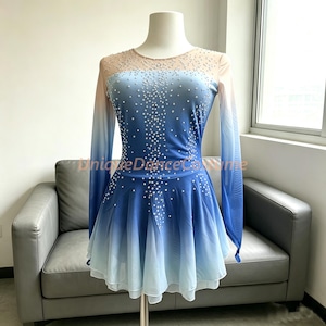 May include: A long-sleeved dance dress featuring an ombre gradient from light blue to white, adorned with scattered clear crystals. The bodice has a sheer nude-colored yoke, and the skirt is layered. The text UniqueDanceCostume is visible.