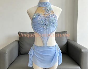 May include: A light blue dance costume featuring a halter neckline, sheer mesh panels, and intricate floral lace appliqués. The bodice and skirt are embellished with clear crystals and beads. The text UniqueDanceCostume is visible across the center.