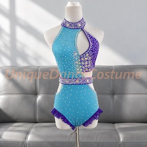 May include: A sleeveless leotard featuring a high neck, a cutout on the upper chest, and a waist band. The garment is decorated with light blue and purple fabric panels, clear rhinestones, and a purple ruffled trim along the leg openings.